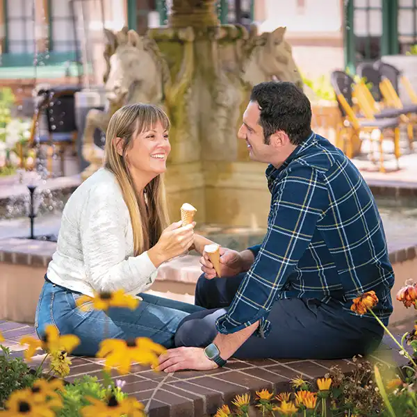 Nicole and Alessio Carnevale sitting in front of a fountain, staring into each others eyes and enjoying a gelato cone.