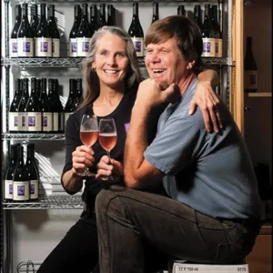 Kate Griffith and Norm Yost sitting amongst bottles of their sparkling wine.