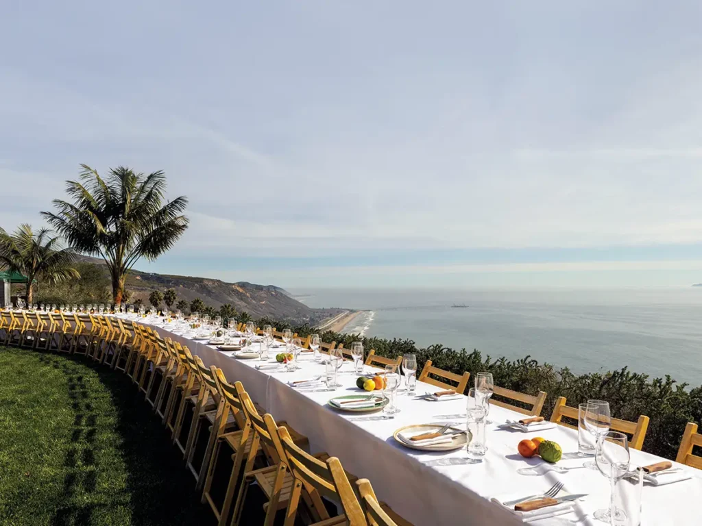 Long winding table with white tablecloth on a bluff high above the Pacific Ocean.
