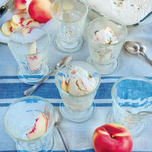Multiple clear dessert cups containing peach and pistachio semifreddo on a blue and white tablecloth.
