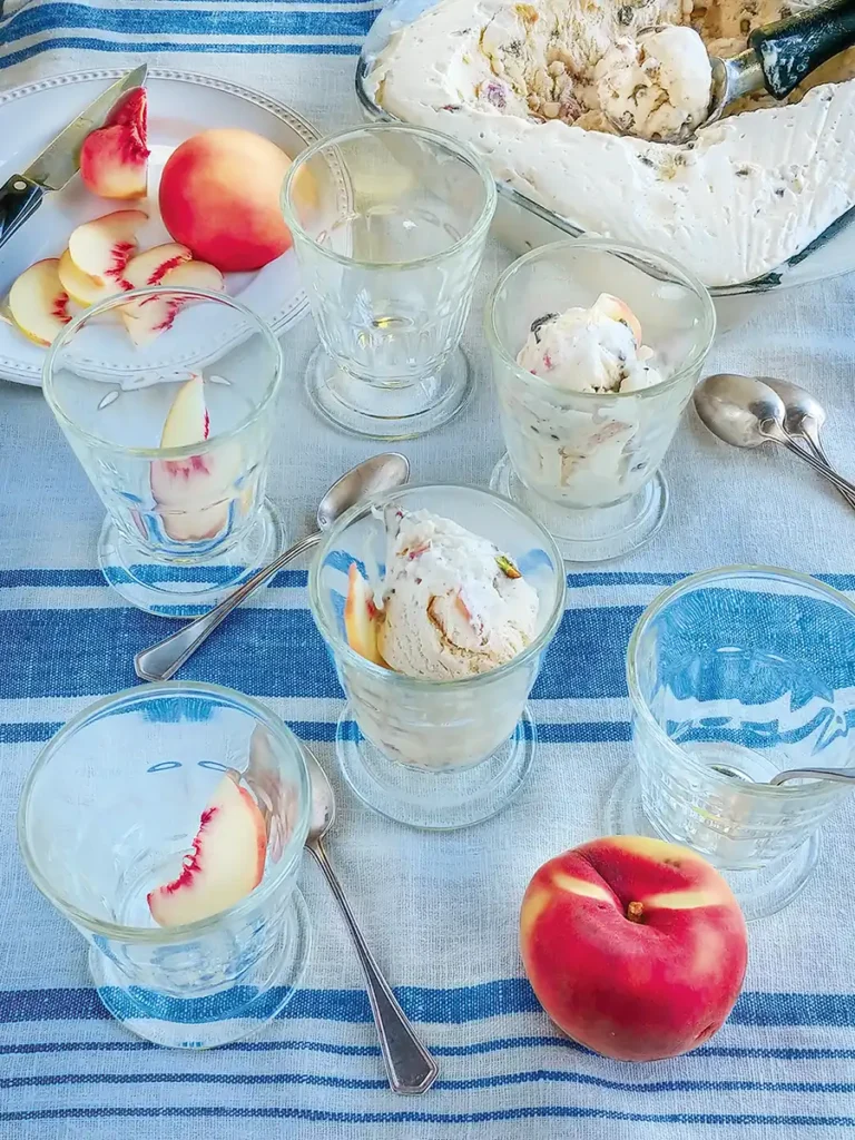 Multiple clear dessert cups containing peach and pistachio semifreddo on a blue and white tablecloth.