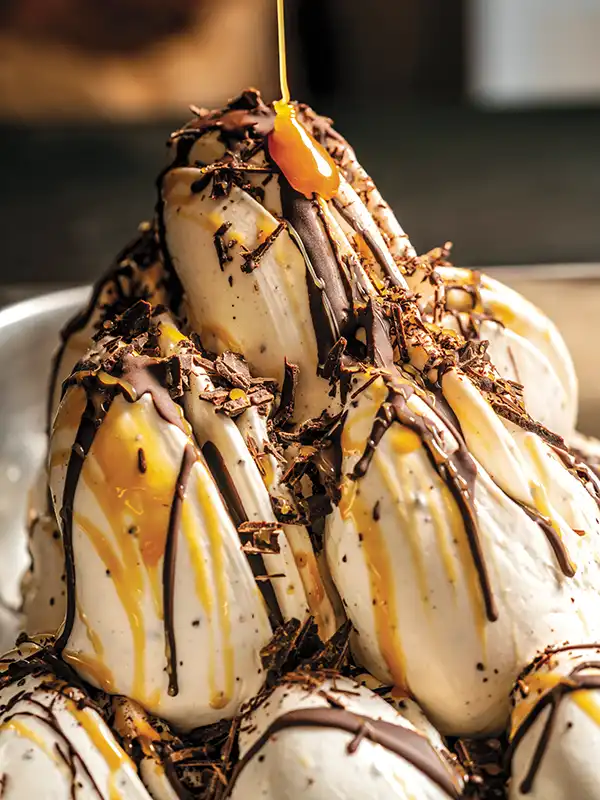 A swirl of Stracciatella gelato in the gelato case with caramel being drizzled on top.