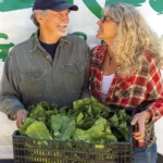 Terry and Holly Delaney stand in front of one of their vans holding a crate full of produce.