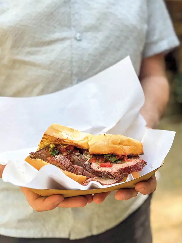 Man holding a trip sandwich in with outstretched arms.
