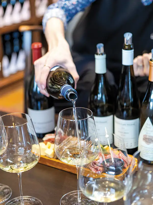 Server pouring a glass of wine while a charcuterie board is visible in the background.
