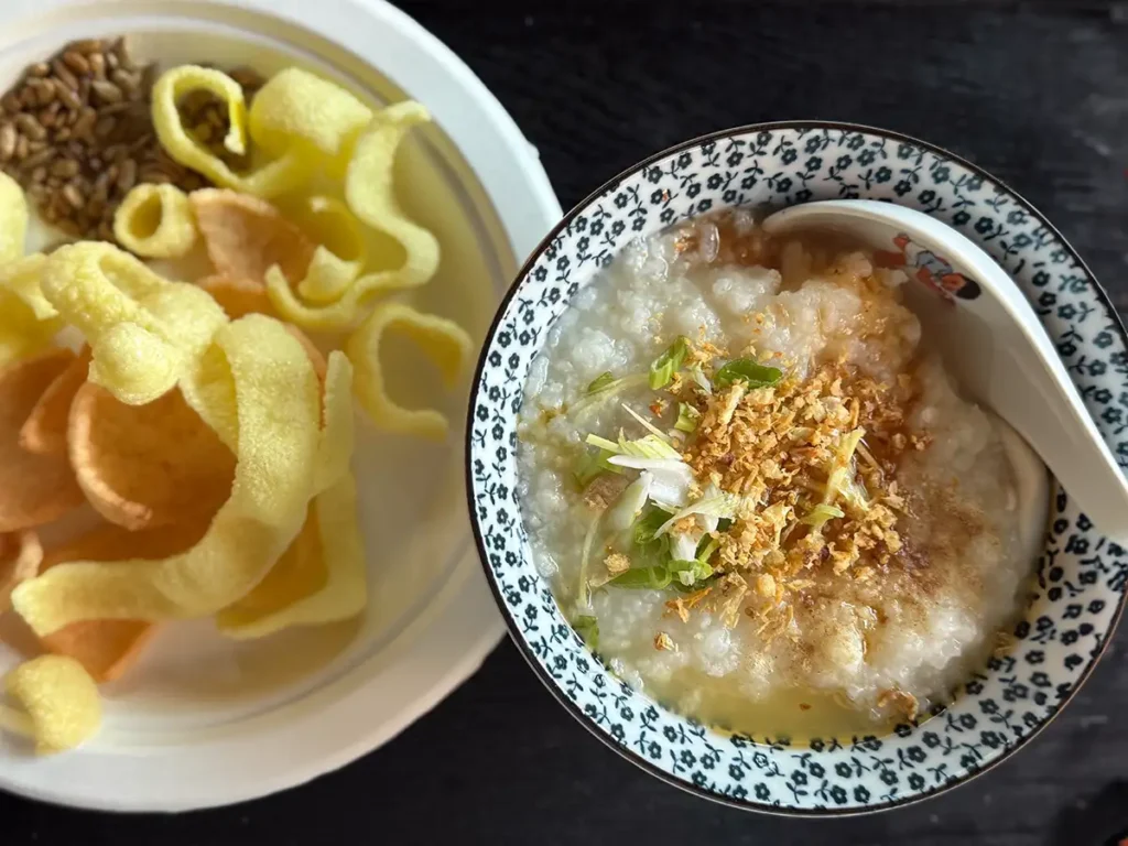A bowl of basic congee next to a plate of shrimp chips.