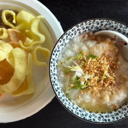 A bowl of basic congee next to a plate of shrimp chips.