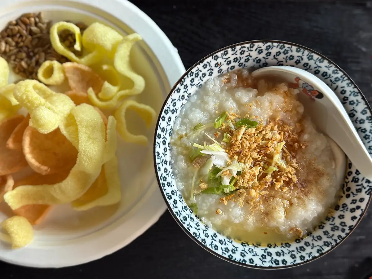 A bowl of basic congee next to a plate of shrimp chips.
