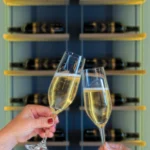 Champagne glasses cheers in front of shelves of bottles.