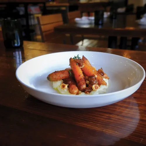 A white plate of roasted Roots Farm carrots with miso brown butter, parsnips, and hazelnuts.
