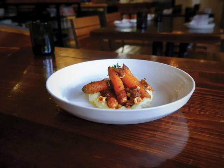 A white plate of roasted Roots Farm carrots with miso brown butter, parsnips, and hazelnuts.