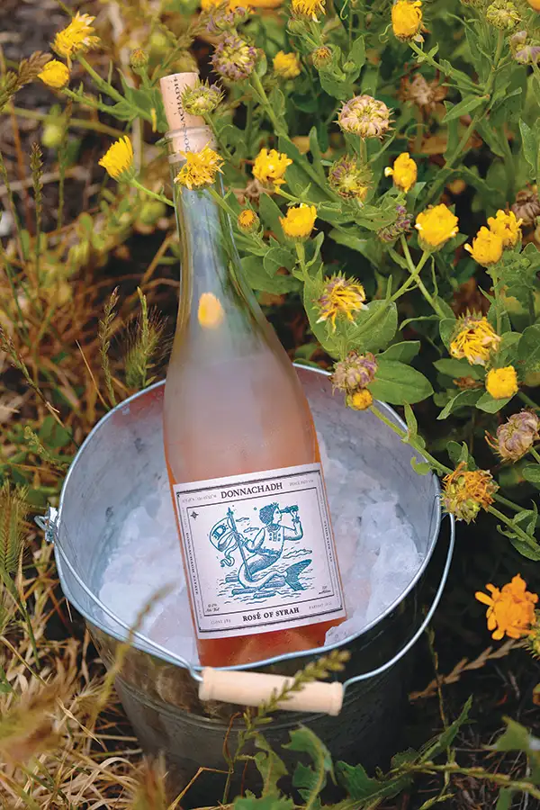 A bottle of rose in an ice bucket, set among flowers.