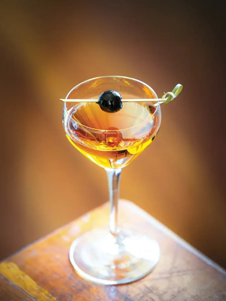 The Old Man Returns in a Nick and Norah glass with a cherry balanced on a toothpick suspended above the drink.