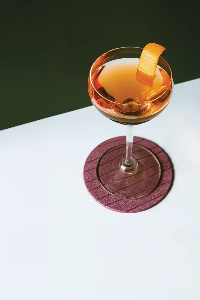 Cocktail coupe with an orange peel garnish against a stark diagonal-divided background.