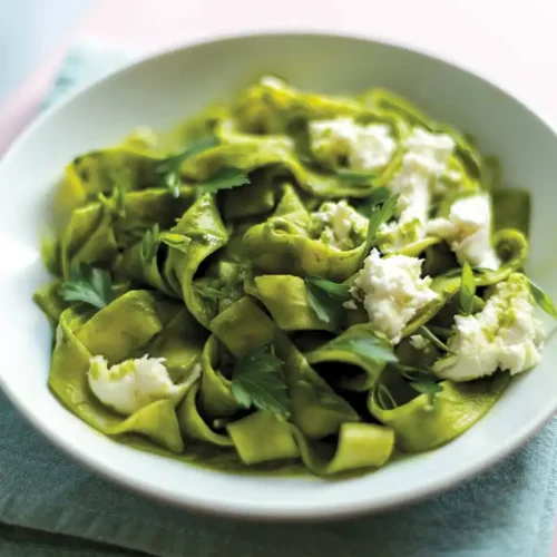 A white bowl with vibrant creamy kale pasta with mozzarella and herbs set on a dish towel.