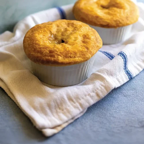 Two individual pot pies set on top of a white tea towlel with a blue stripe.