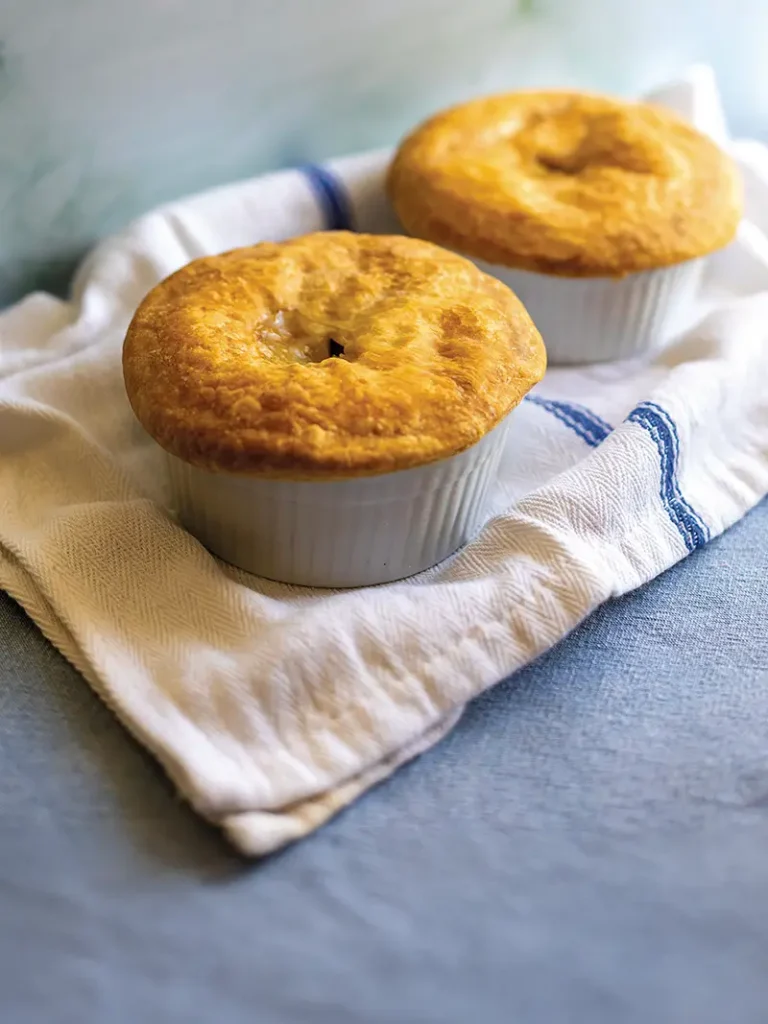 Two individual pot pies set on top of a white tea towlel with a blue stripe.