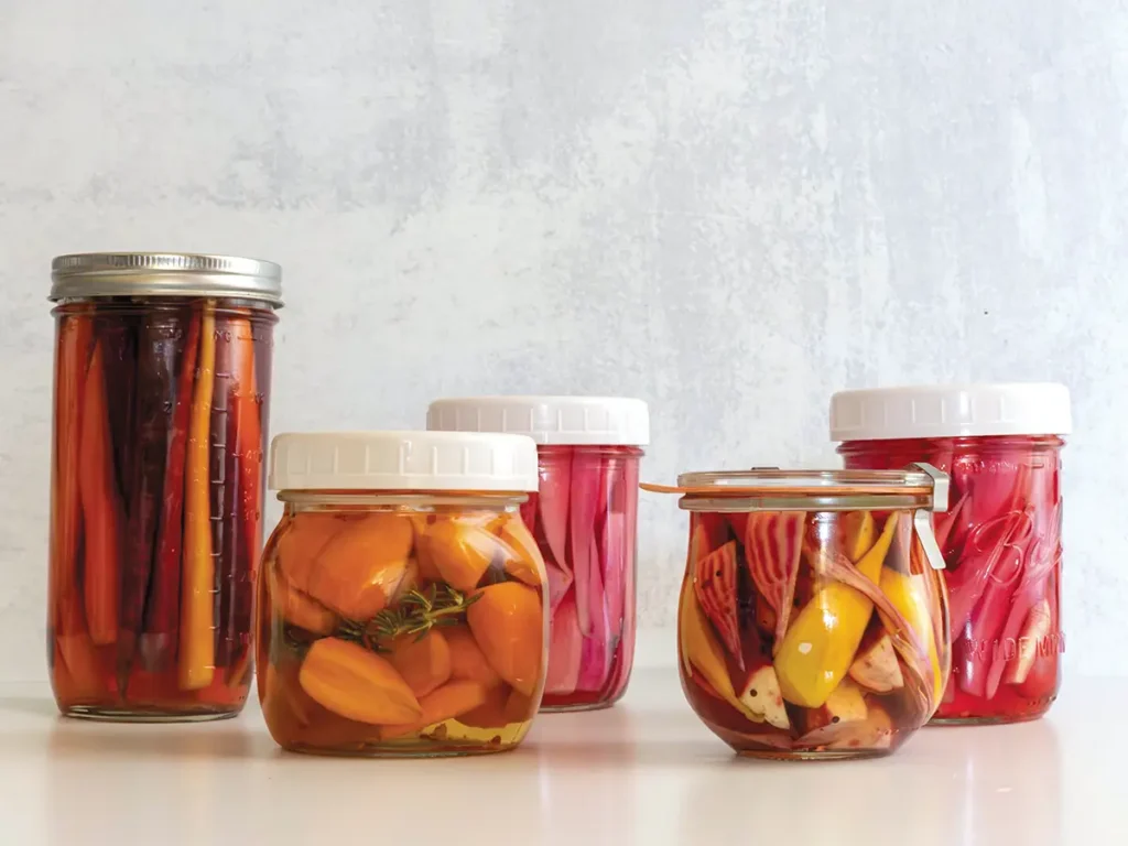 Five jars of assorted refrigerator pickles on a counter.