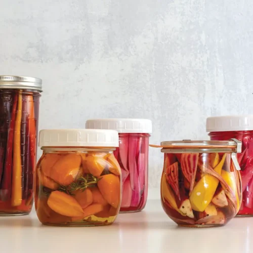 Five jars of assorted refrigerator pickles on a counter.