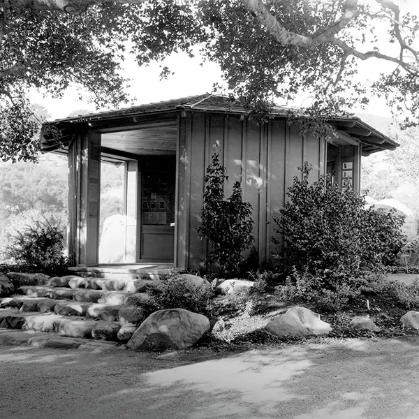 A small visitor center nestled beneath mature oak trees welcomes guests to the Santa Barbara Botanic Garden with rustic architecture that blends into the surrounding landscape.