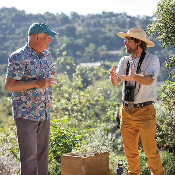 A Santa Barbara Botanic Garden naturalist speaks with a visitor while discussing native plants against the backdrop of the Garden's rolling hills and woodlands.