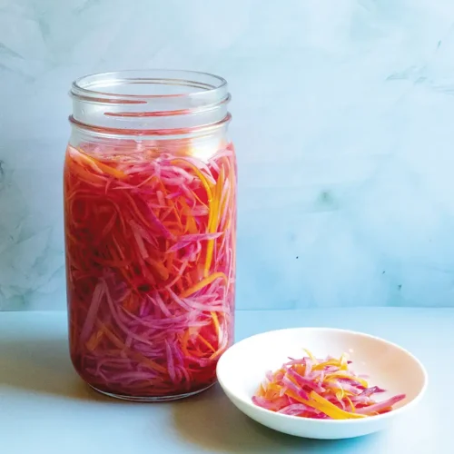 Vietnamese Quick-Pickled Daikon & Carrots (Đo Chua) in a mason jar with a shallow white dish containing some of the pickle next to it.