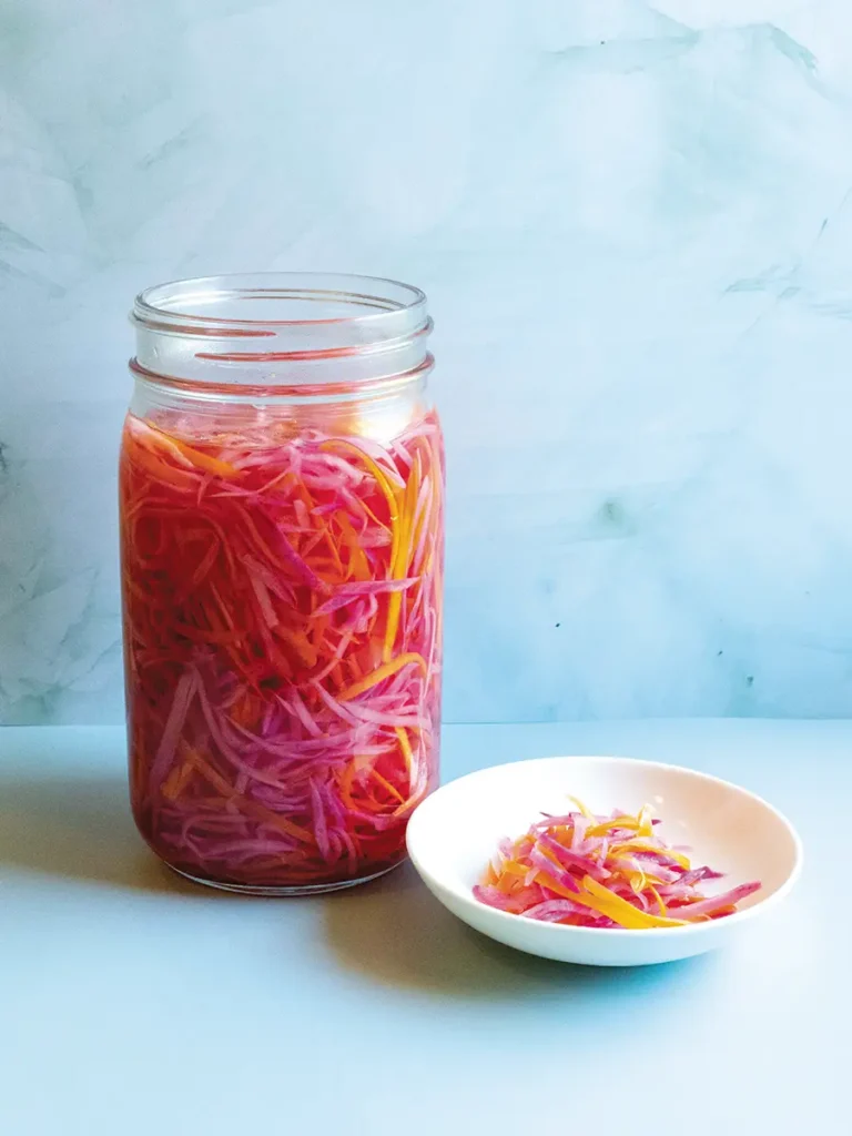 Vietnamese Quick-Pickled Daikon & Carrots (Đo Chua) in a mason jar with a shallow white dish containing some of the pickle next to it.