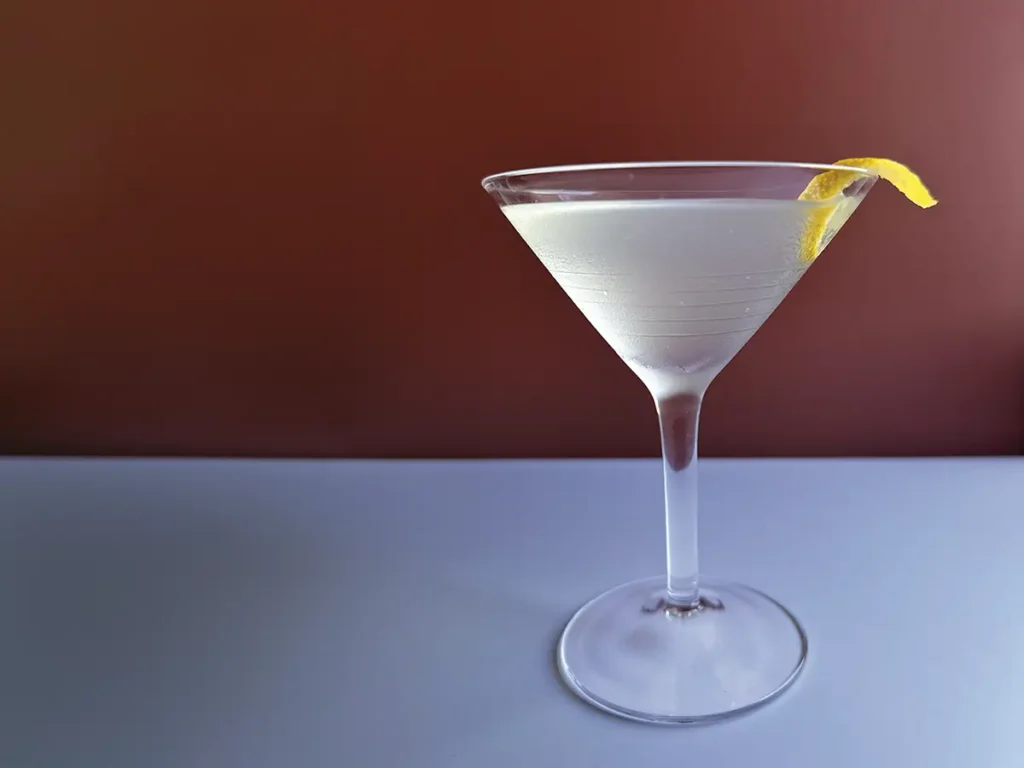Martini glass with a lemon twist against a red background.