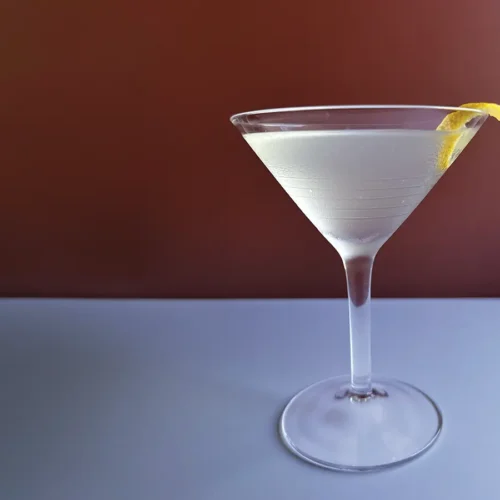 Martini glass with a lemon twist against a red background.
