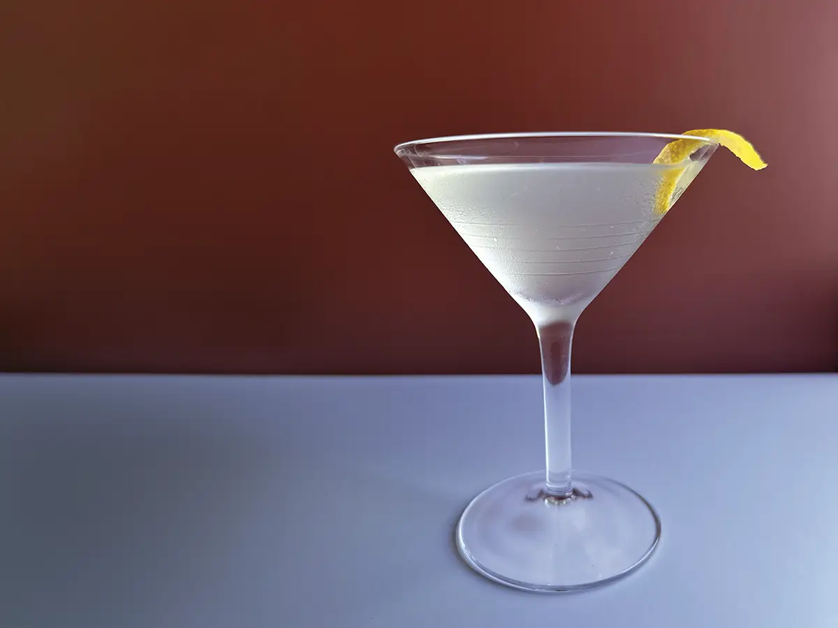 Martini glass with a lemon twist against a red background.