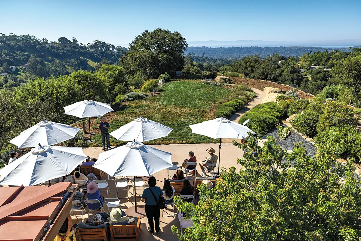 Visitors gather under white umbrellas for an outdoor presentation overlooking the scenic landscapes and native plant gardens of the Santa Barbara Botanic Garden.