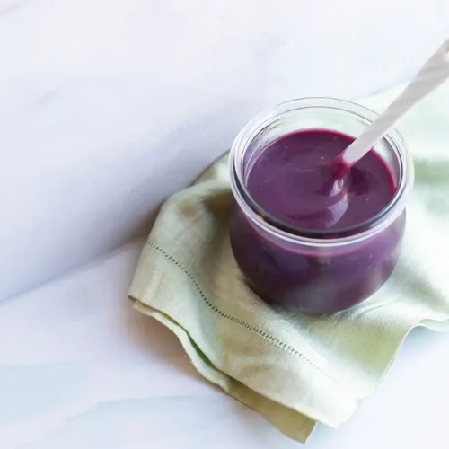 Pot of blueberry lemon curd on a dish towel set against a marble counter and backsplash.