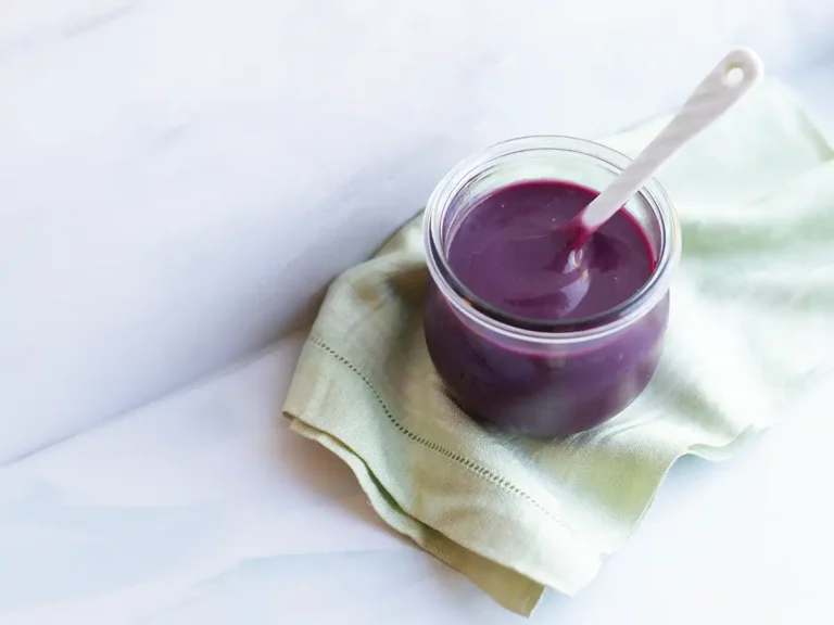 Pot of blueberry lemon curd on a dish towel set against a marble counter and backsplash.