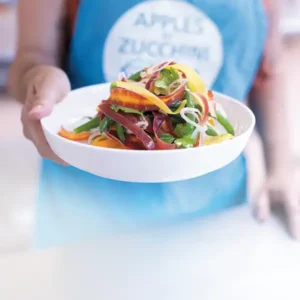 Woman holding forward a plate of carrot ribbons and green bean salad.
