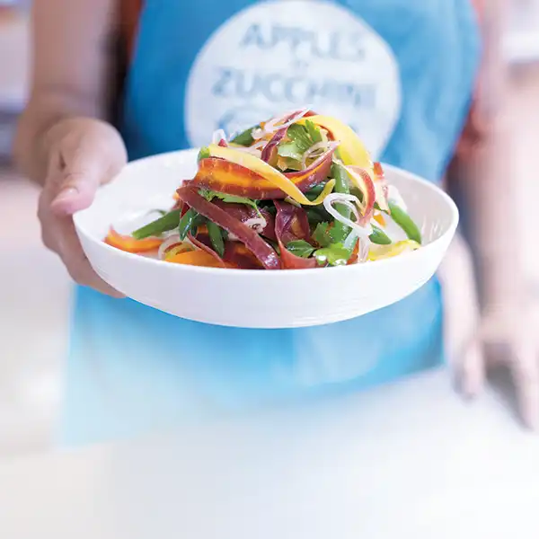 Woman holding forward a plate of carrot ribbons and green bean salad.