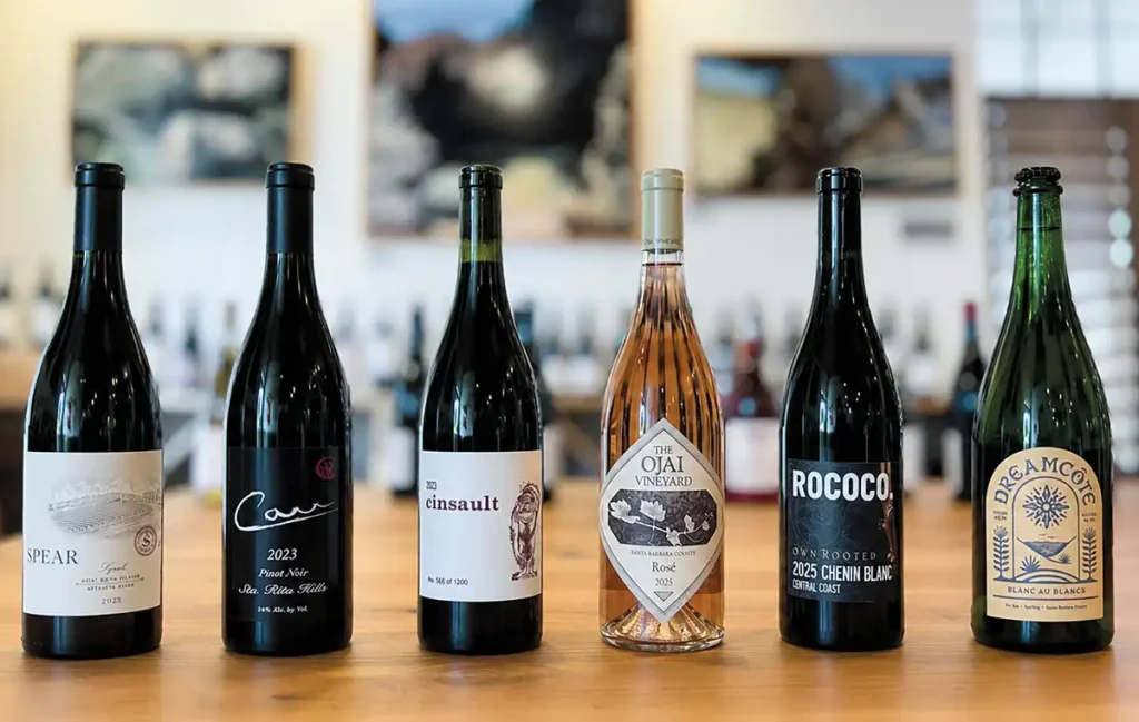Lineup of 6 bottles of local wine on a wood tabletop.
