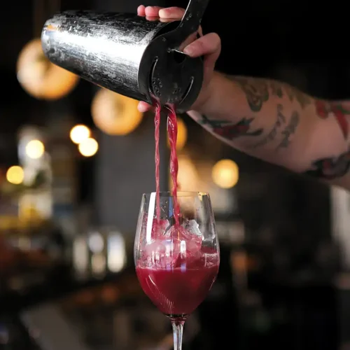 Bartender pours from a shaker into a waiting wine glass.