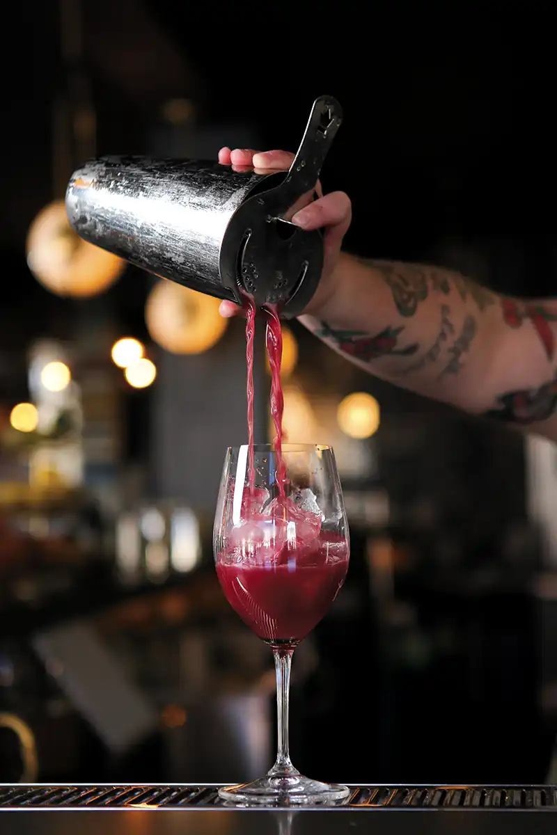 Bartender pours from a shaker into a waiting wine glass.