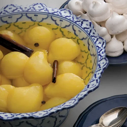 Bowl of Poached Pears with Saffron next to a plate of meringues.