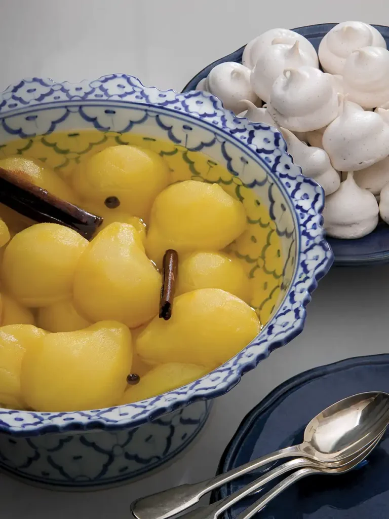 Bowl of Poached Pears with Saffron next to a plate of meringues.
