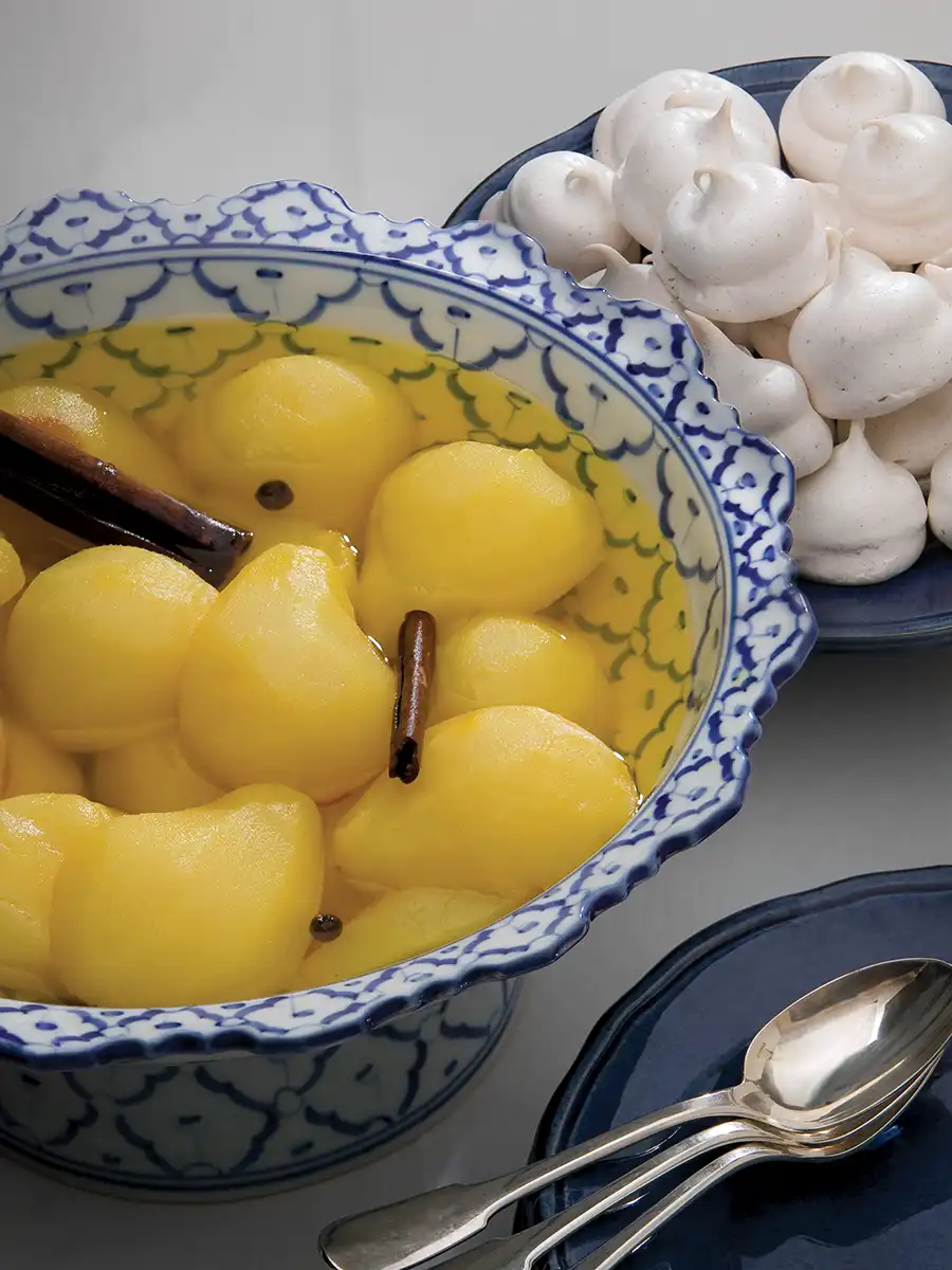 Bowl of Poached Pears with Saffron next to a plate of meringues.