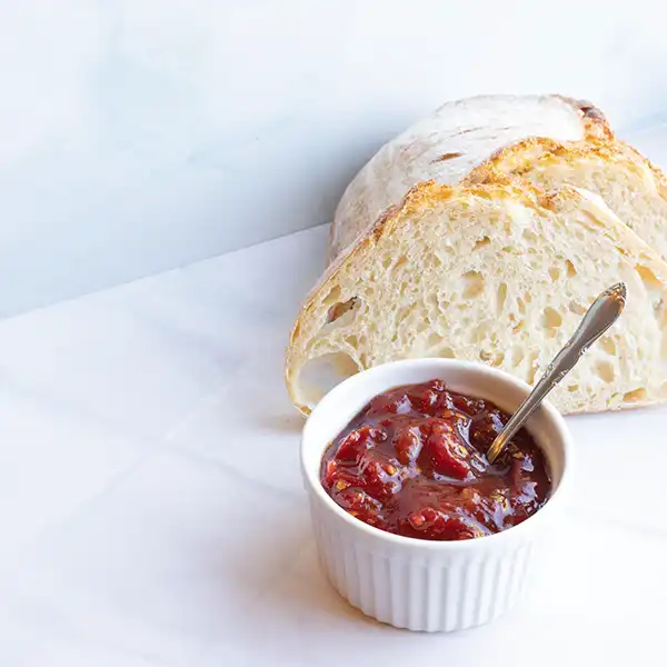 Sourdough slices sit behind a white ramekin filled with Tomato Jam with Ginger.